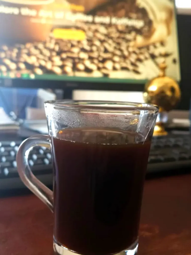 A hot cup of Americano coffee on a desk in front of a computer, showcasing the smooth and rich look of What Is An Americano.