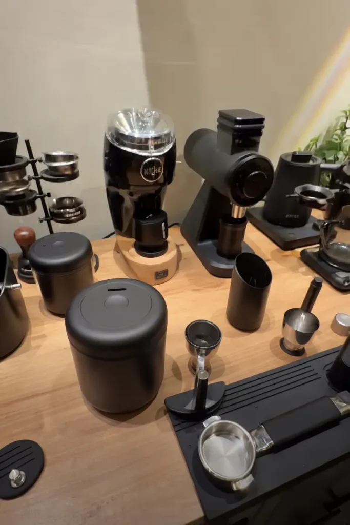Full home barista espresso setup on a wooden countertop featuring the Simple Modern Delta coffee canister in matte black for bean storage, alongside the Niche Duo flat burr grinder, portafilter, dosing tools, and a complete collection of espresso accessories for a precision manual brewing workflow.