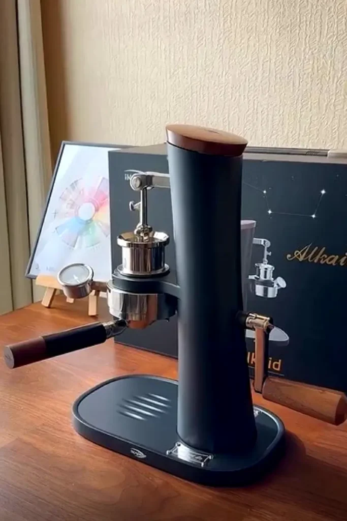 IKAPE Alkaid hand-cranked manual espresso machine in matte black with walnut wood accents and chrome portafilter, displayed on a wooden countertop next to its premium packaging box.