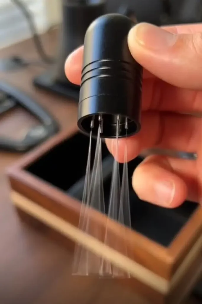 Hand holding the IKAPE WDT Tool with ultra-fine 0.25mm needles extended, showing the precise needle cluster used for the wdt tool espresso distribution technique β one of the most essential espresso tools for eliminating channeling and improving extraction consistency.